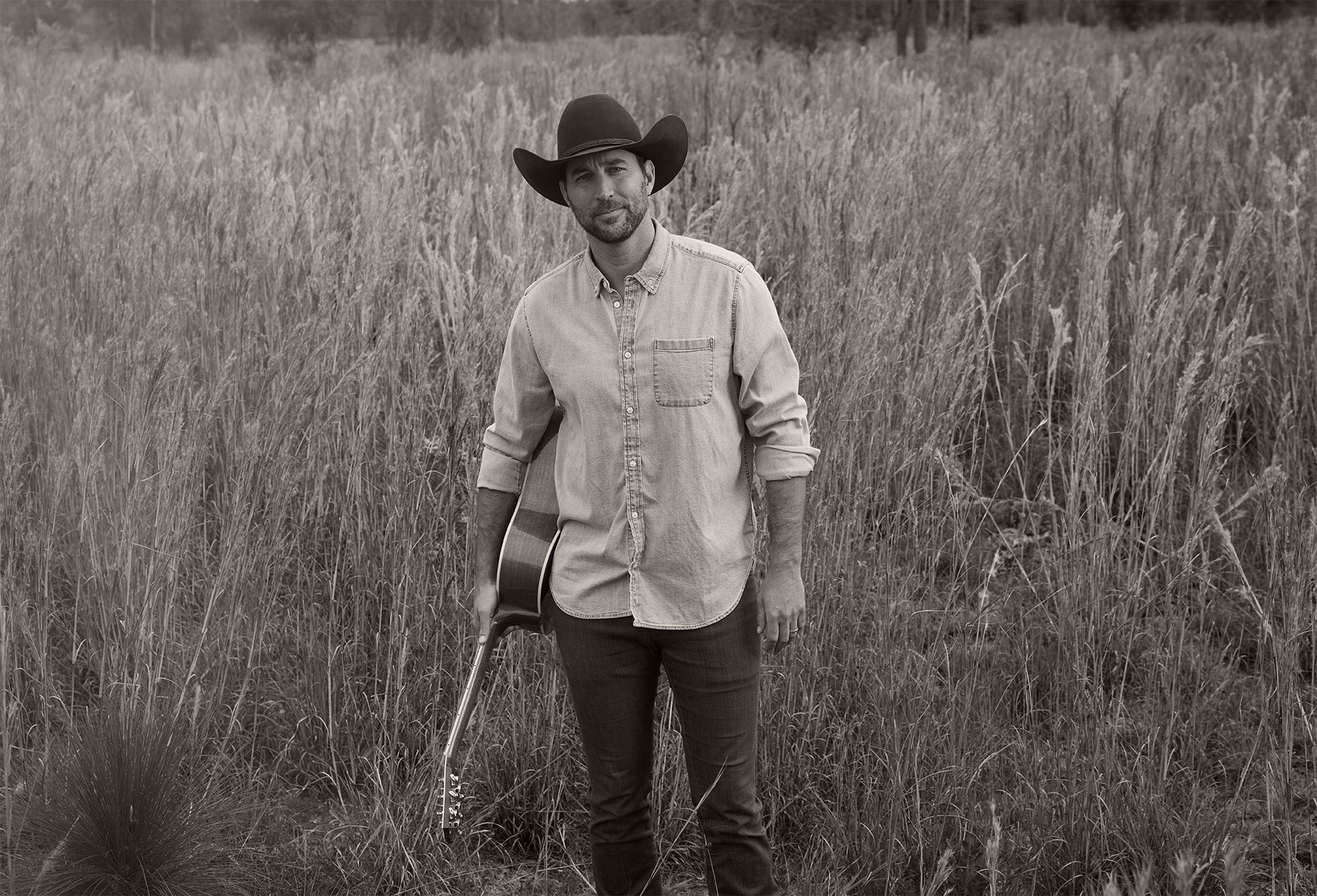 Photo with a sepia filter of Adam in a field with his guitar